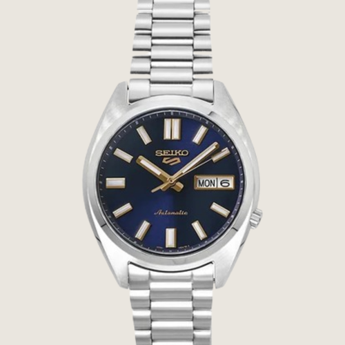 Seiko 5 Sports SNXS SRPL55K1, navy sunburst dial with gold accents and steel bracelet, on a plain bone background