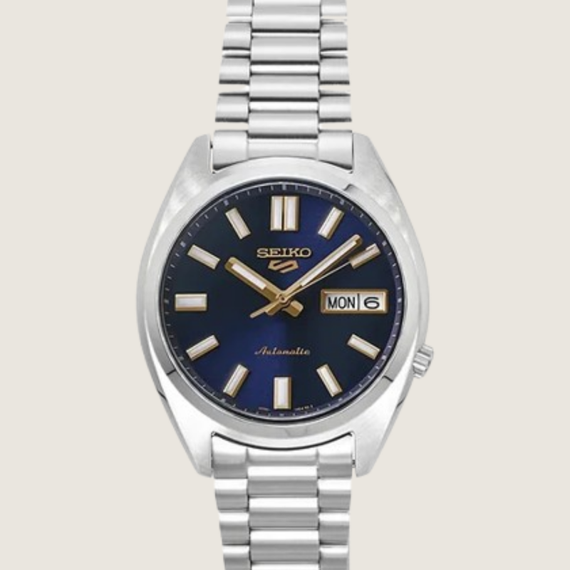 Seiko 5 Sports SNXS SRPL55K1, navy sunburst dial with gold accents and steel bracelet, on a plain bone background