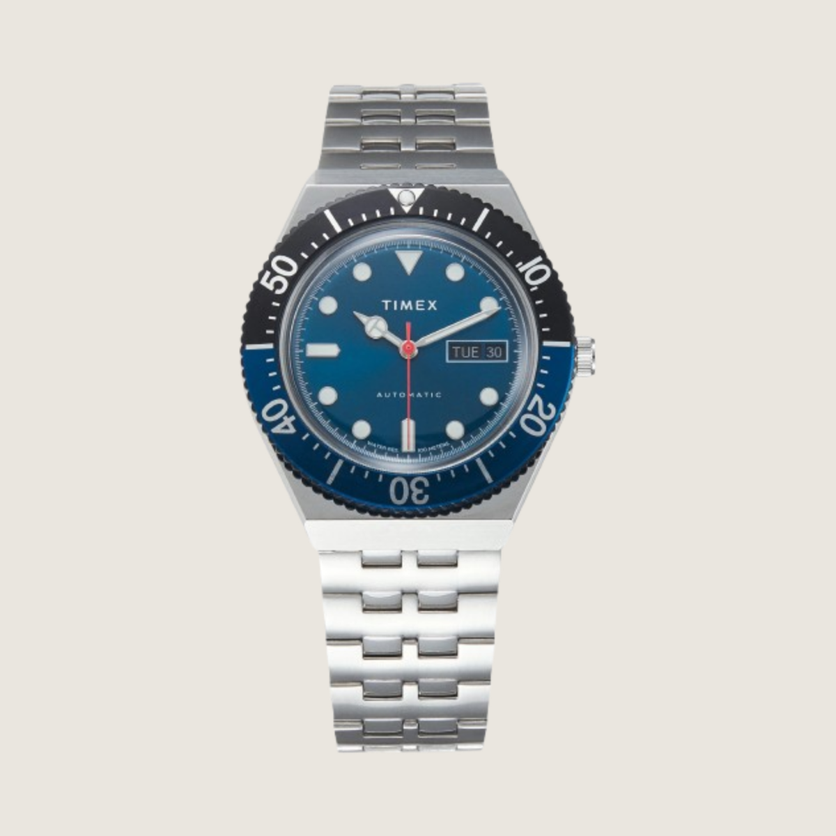 Timex Blueberry Automatic diver with navy bezel, blue dial and stainless steel bracelet, on a plain bone background