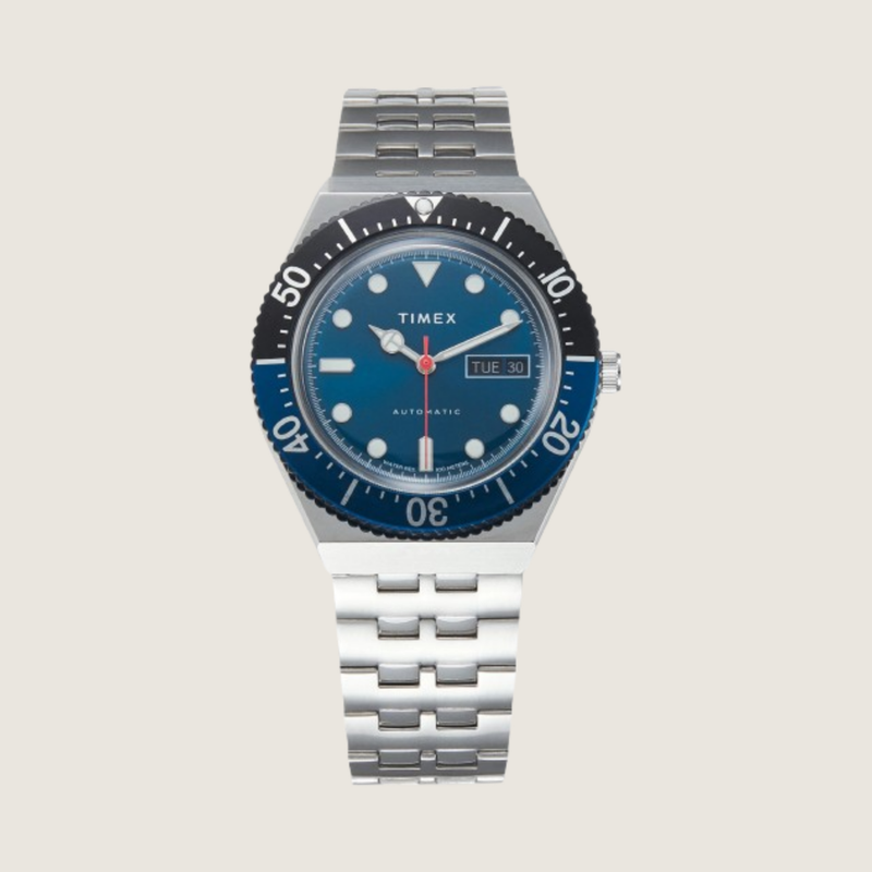 Timex Blueberry Automatic diver with navy bezel, blue dial and stainless steel bracelet, on a plain bone background